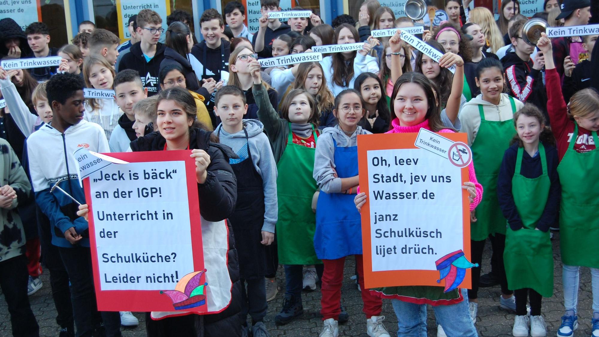 Schüler stehen vor der Schule und halten Protestschilder hoch.