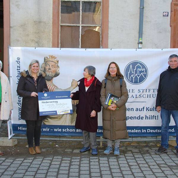Fünf Personen stehen vor einem Haus, an dessen Fassade Plakate hängen.