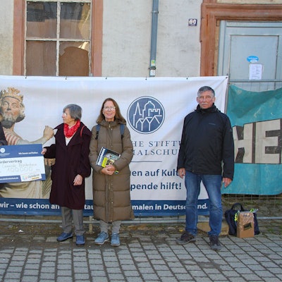 Fünf Personen stehen vor einem Haus, an dessen Fassade Plakate hängen.