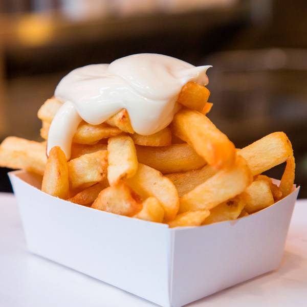 Eine Portion Pommes Frittes mit Mayonaise steht auf einem Tisch.