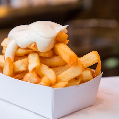 Eine Portion Pommes Frittes mit Mayonaise steht auf einem Tisch.