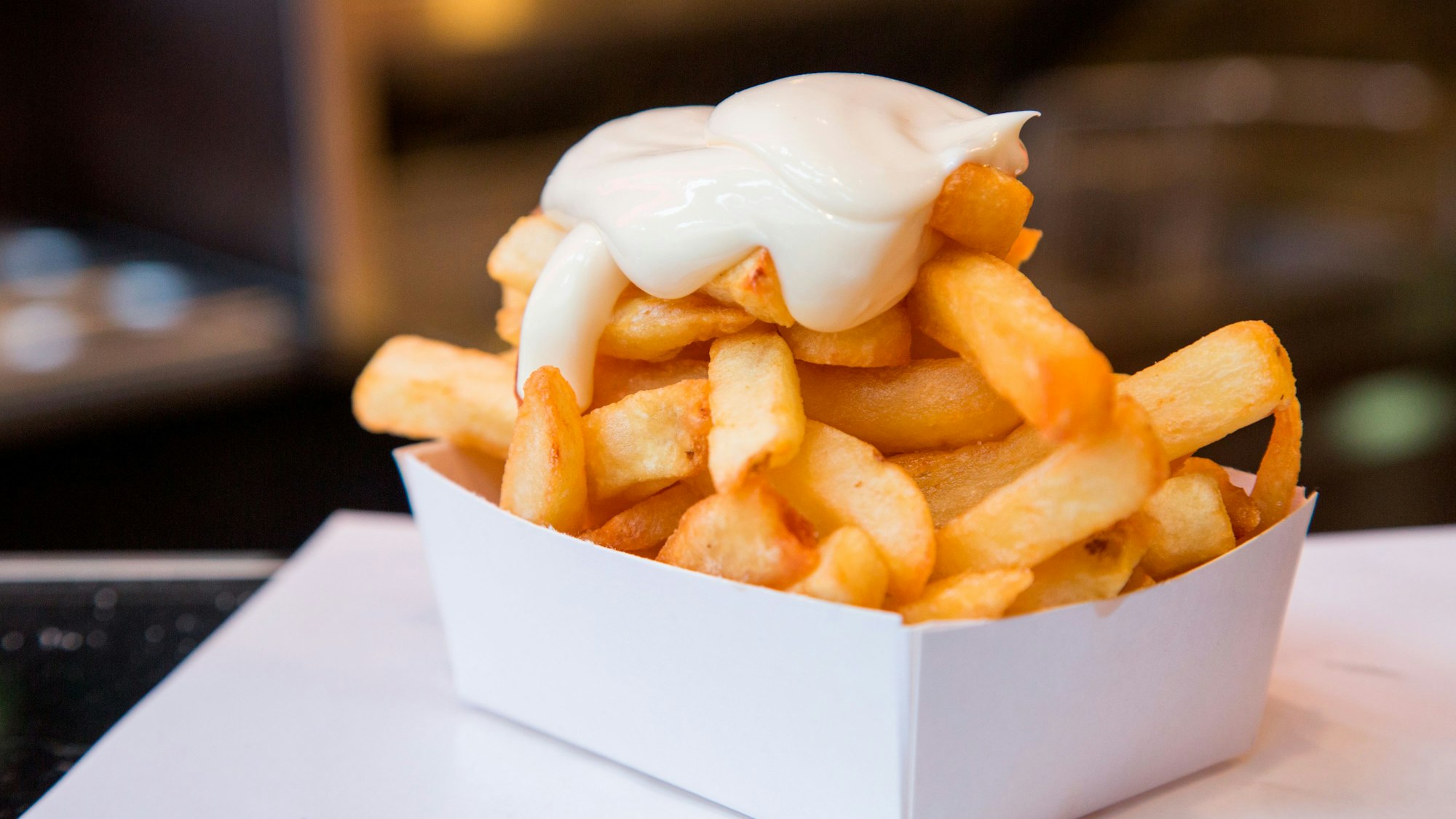Eine Portion Pommes Frittes mit Mayonaise steht auf einem Tisch.
