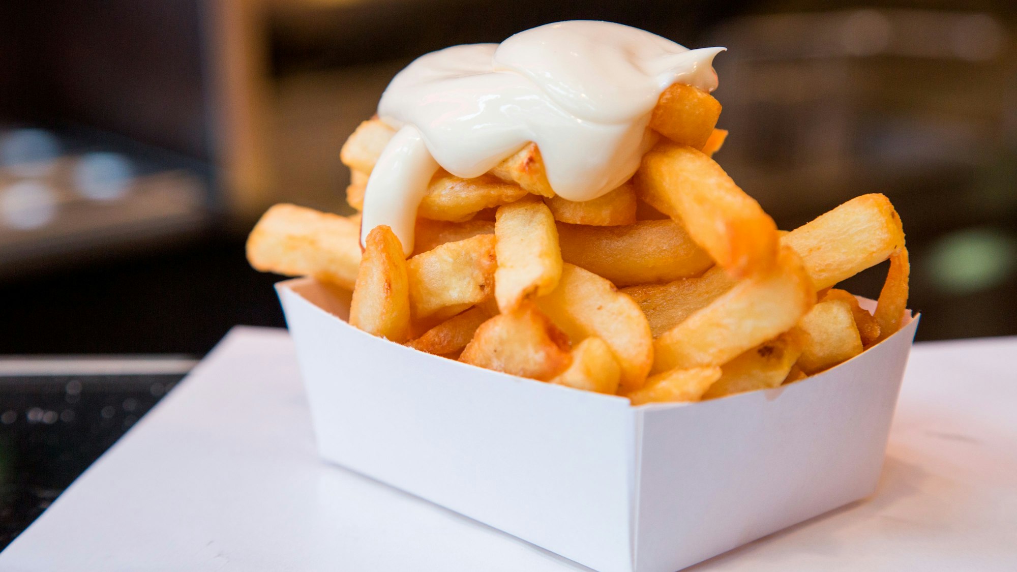 Eine Portion Pommes Frittes mit Mayonaise steht auf einem Tisch.