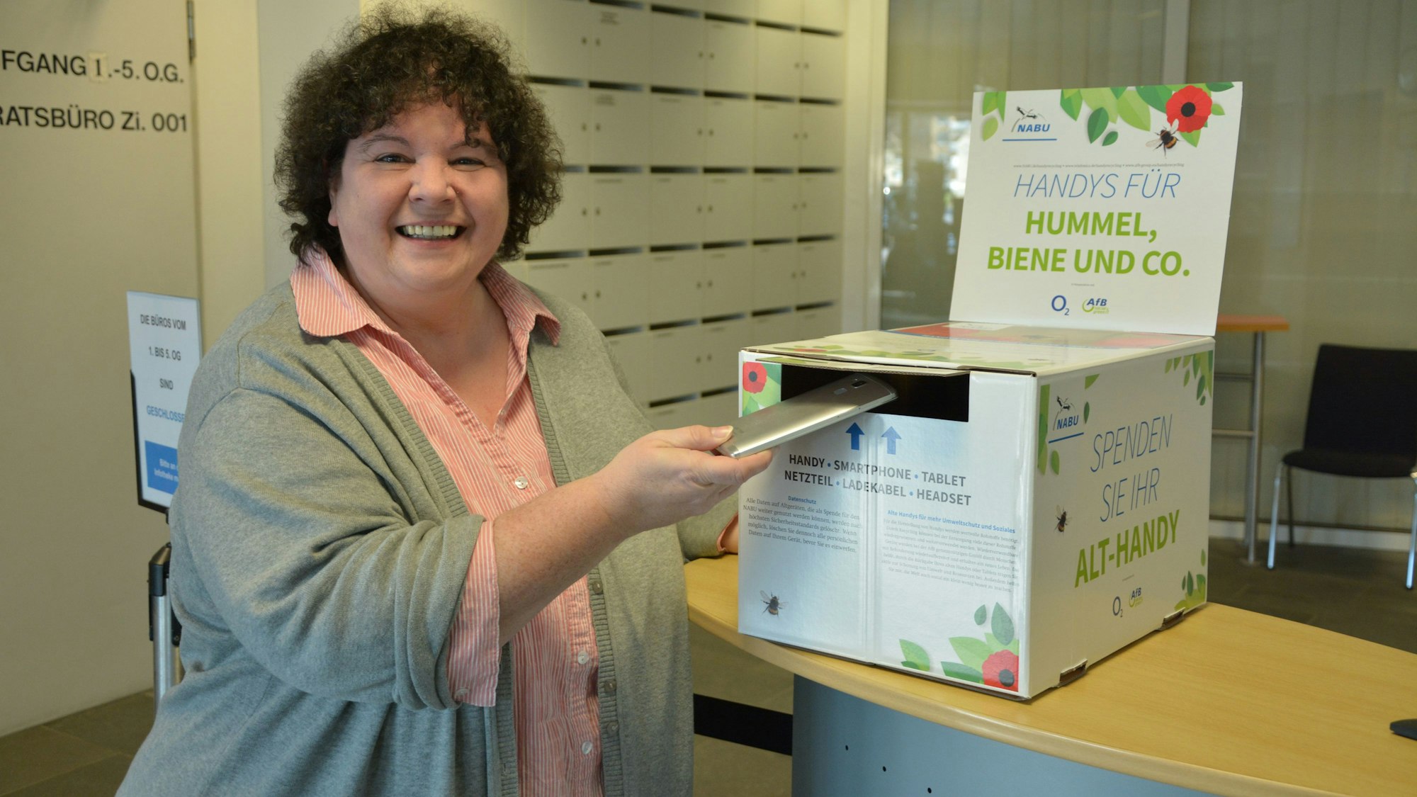 Klimaschutzmanagerin Monika Meves wirft ein Handy in die Sammelbox des Nabu im Leichlinger Rathausfoyer ein.