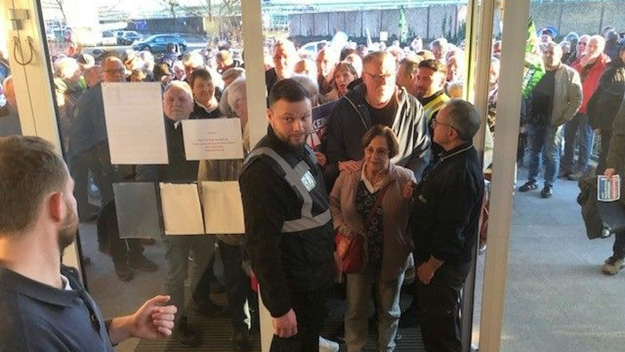 Hunderte Menschen stehen am Eingang zur Bürgerhalle Wiesdorf. Sicherheitskräfte stehen an einem schmalen Eingang und warten darauf, die ersten Wartenden, eine ältere Frau und ihren Mann, einzulassen.