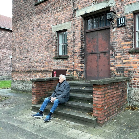Dany Dattel sitzt auf der Treppe vor Block 10 im Stammlager Auschwitz.