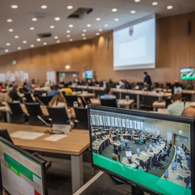 Blick in den Ratssaal, im Vordergrund ein Monitor, der das Bild der Live-Übertragung zeigt.