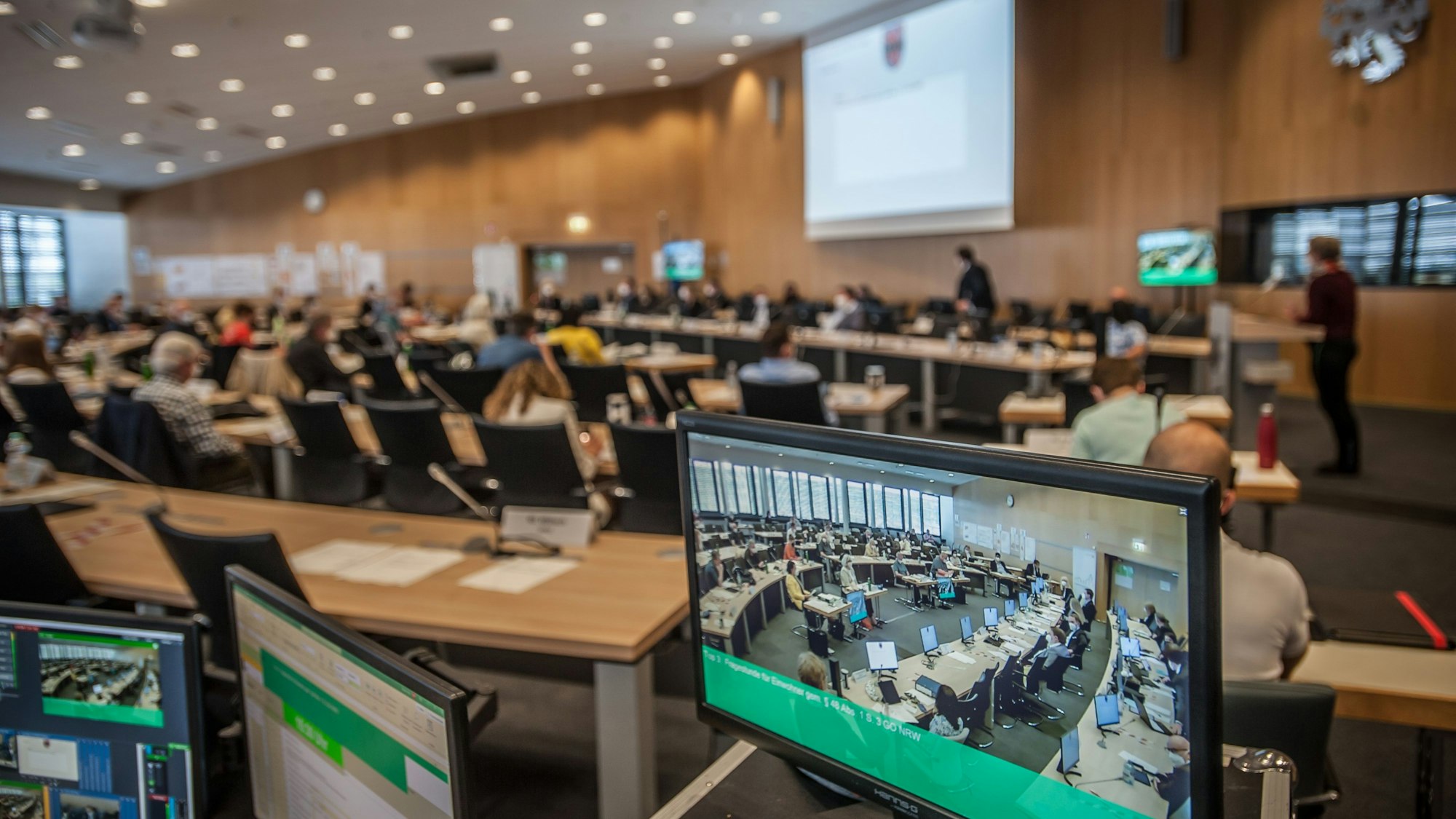 Blick in den Ratssaal, im Vordergrund ein Monitor, der das Bild der Live-Übertragung zeigt.
