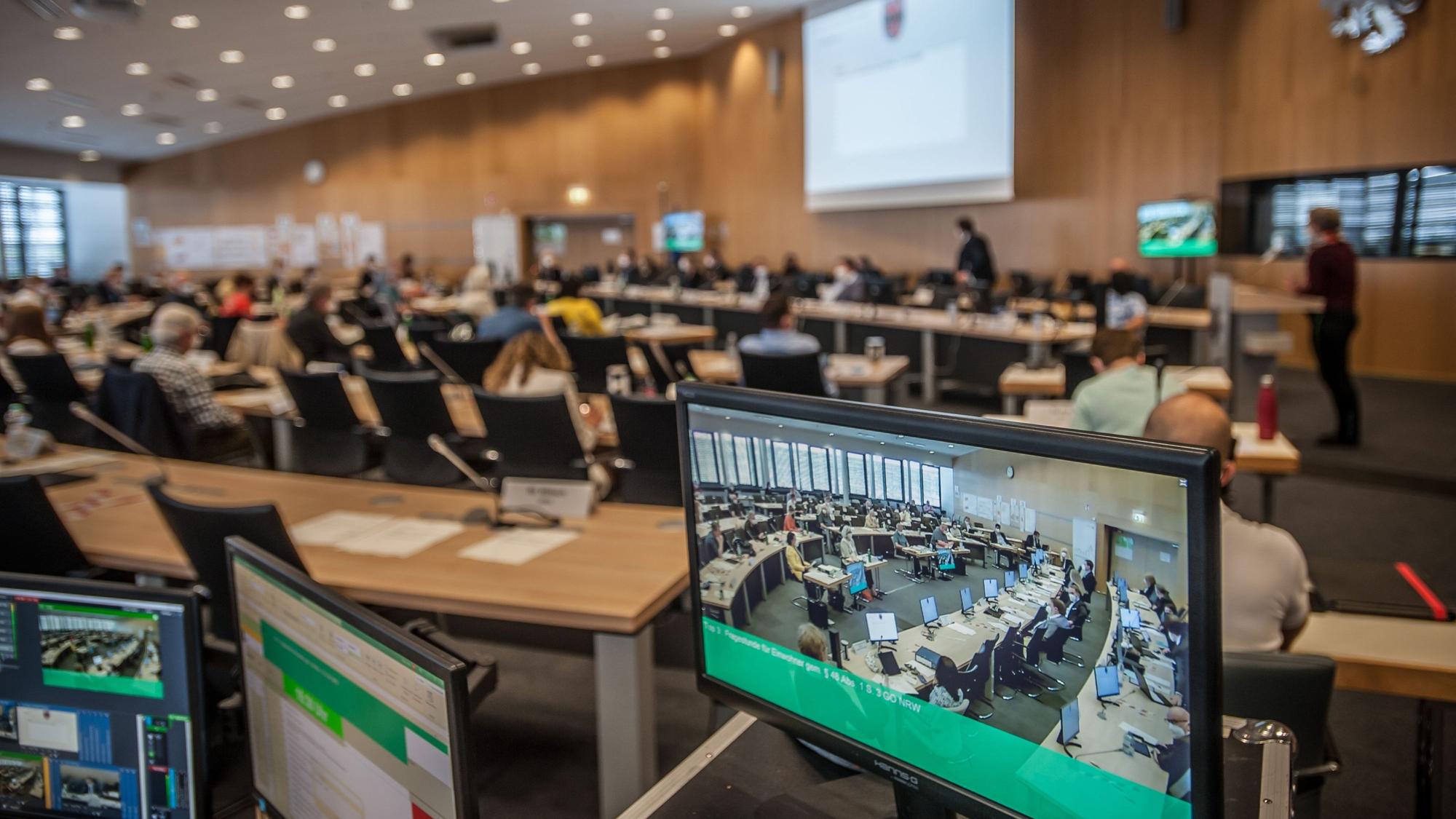 Der Leverkusener Ratssaal mit Bildschirmen im Vordergrund, auf denen die Übertragung zu sehen ist
