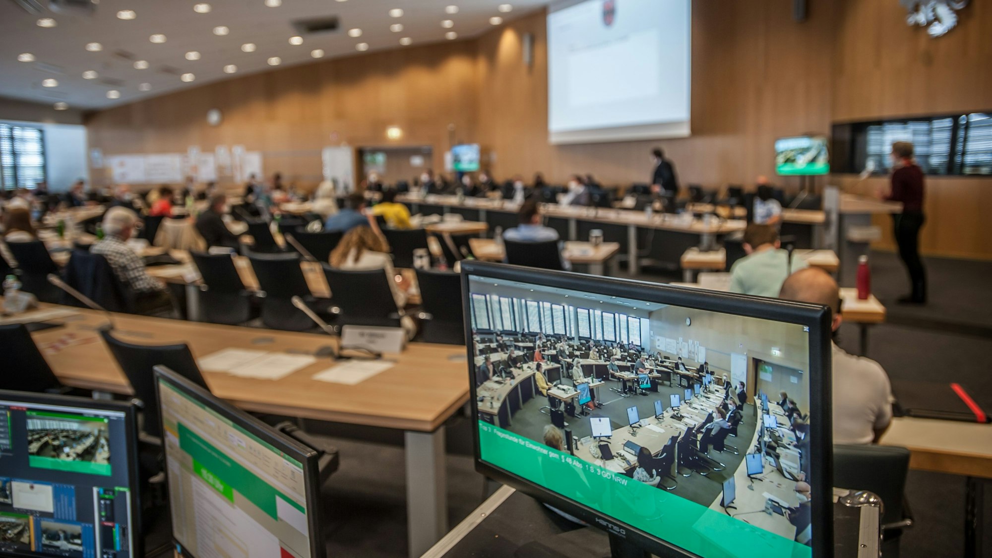 Der Leverkusener Ratssaal mit Bildschirmen im Vordergrund, auf denen die Übertragung zu sehen ist
