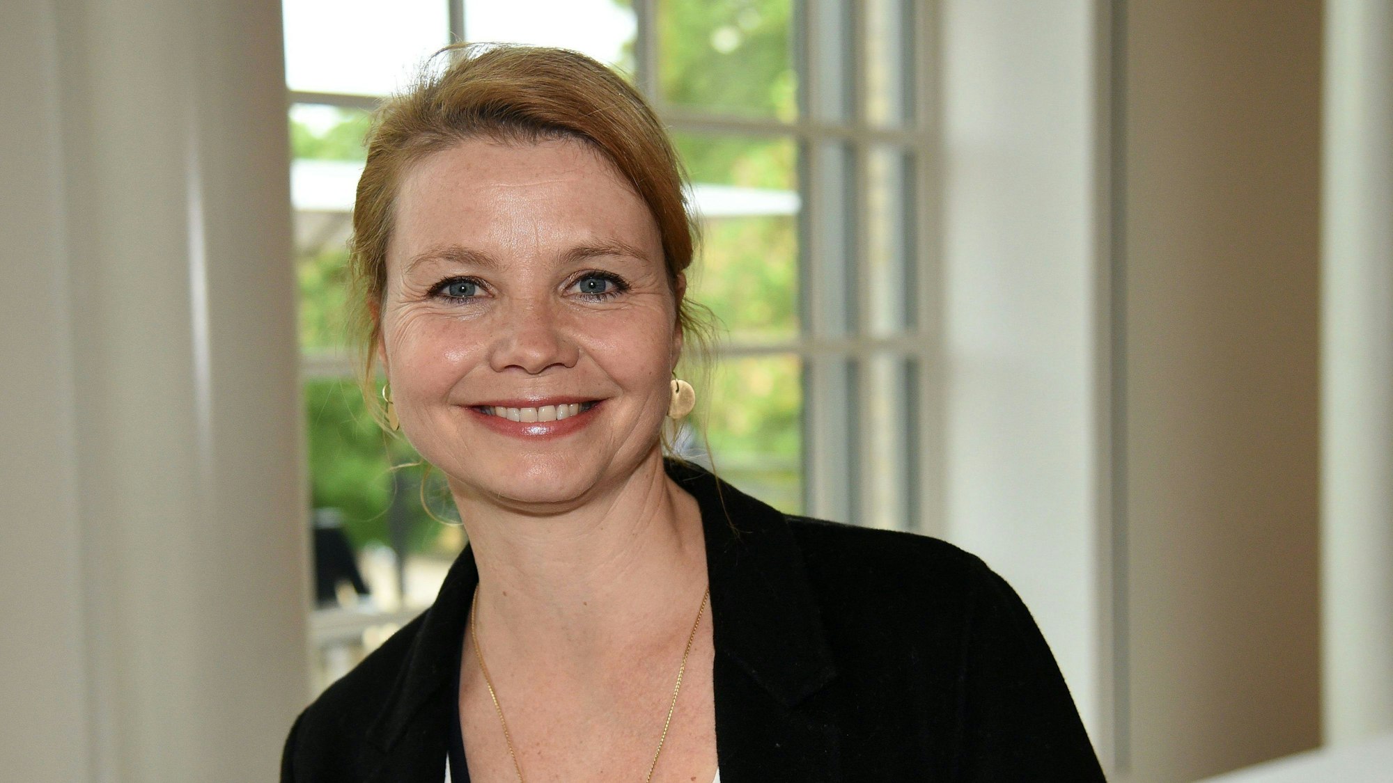 Schauspielerin Annette Frier steht in der Kölner Flora, sie lacht in die Kamera und trägt einen schwarzen Blazer
