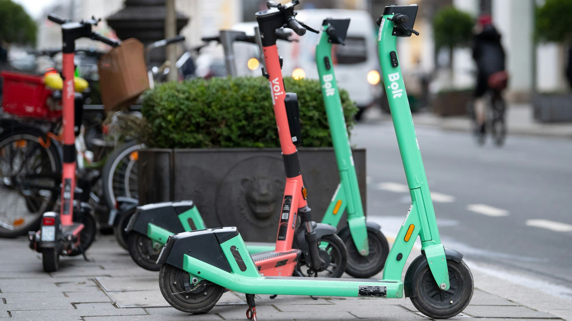 Vier E-Scooter stehen auf einem Gehweg.