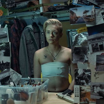 Der blonde Jonathan Perleth hat sich die Brust mit Bandagen abgebunden, sitzt ansonsten oberkörperfrei vor dem Spiegel. Um den Spiegel herum sind viele Postkarten und Fotos.