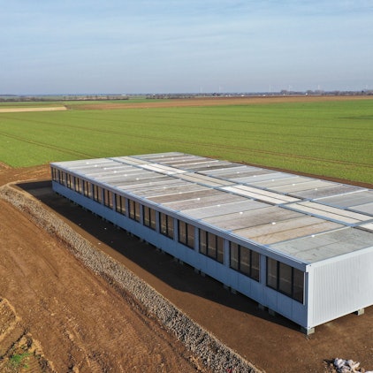Man sieht einen großen Containerbau, umgeben von Feld.