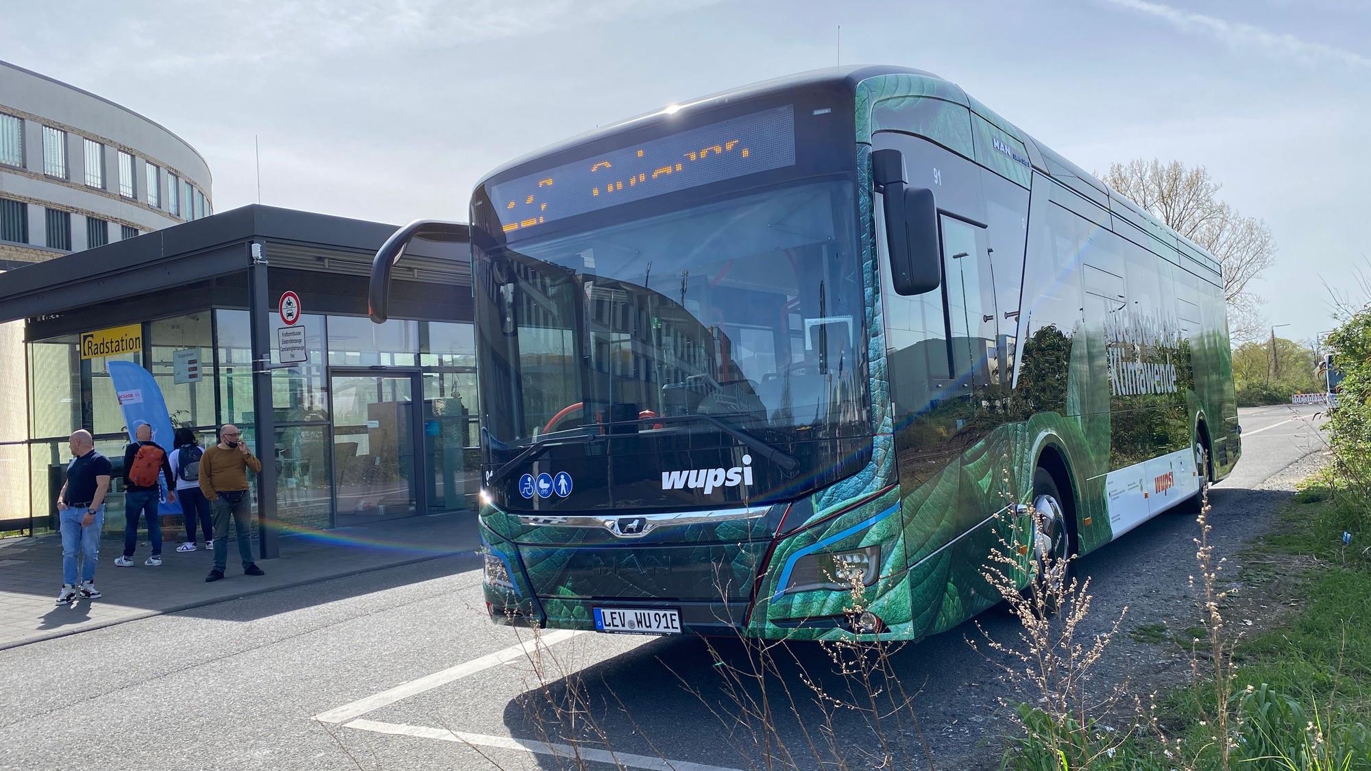 Ein grüner Wupsi-Bus steht an einer Haltestelle.