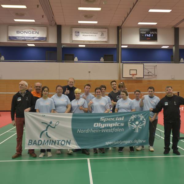 Man sieht das Team, wie es in einer Turnhalle hinter dem Teambanner steht und es zusammen hochhält.