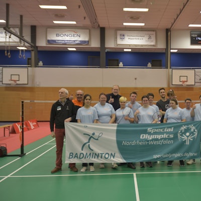 Man sieht das Team, wie es in einer Turnhalle hinter dem Teambanner steht und es zusammen hochhält.