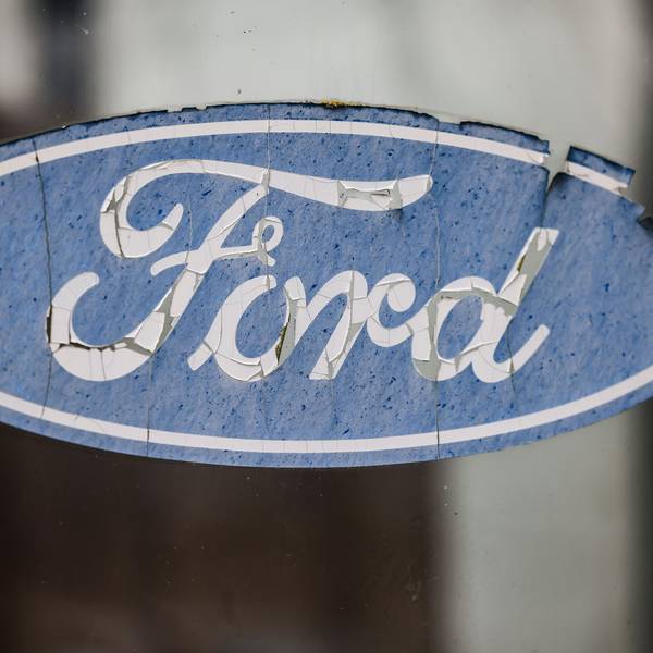 Ein abgeblättertes Logo von Ford hängt an einer Scheibe vor dem Werksgelände.