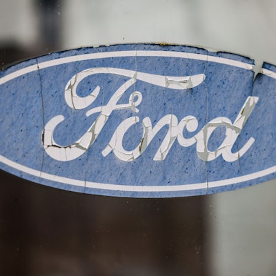 Ein abgeblättertes Logo von Ford hängt an einer Scheibe vor dem Werksgelände.