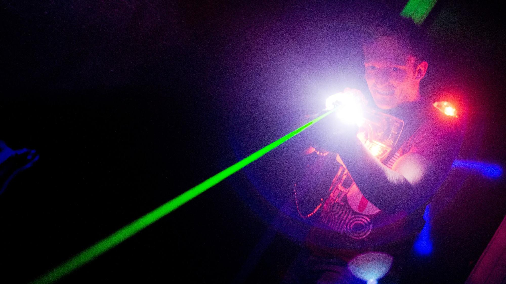 Ein Mann hat eine Waffe in der Hand, aus der ein grüner Laser schießt.