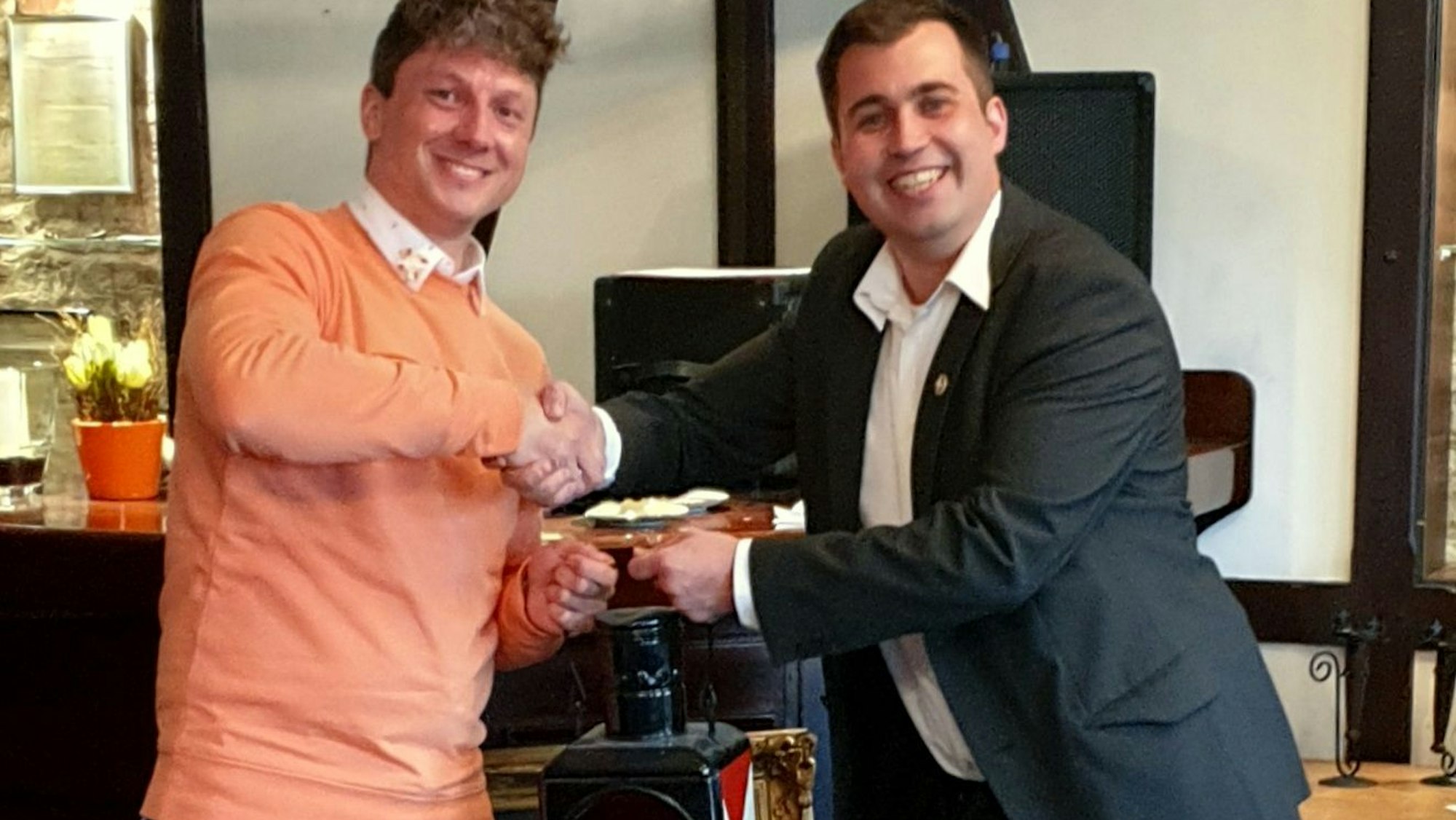 Daniel Weber (links) und Tom Pfeiffer (rechts) halten gemeinsam eine Zuglaterne in der Hand und geben sich die Hand