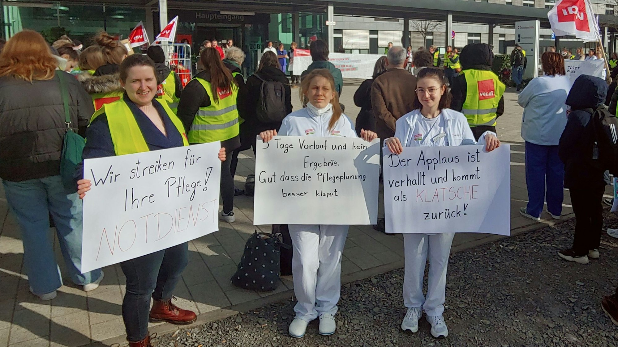 Klinikmitarbeiterinnen mit Schildern vor dem Klinikgelände
