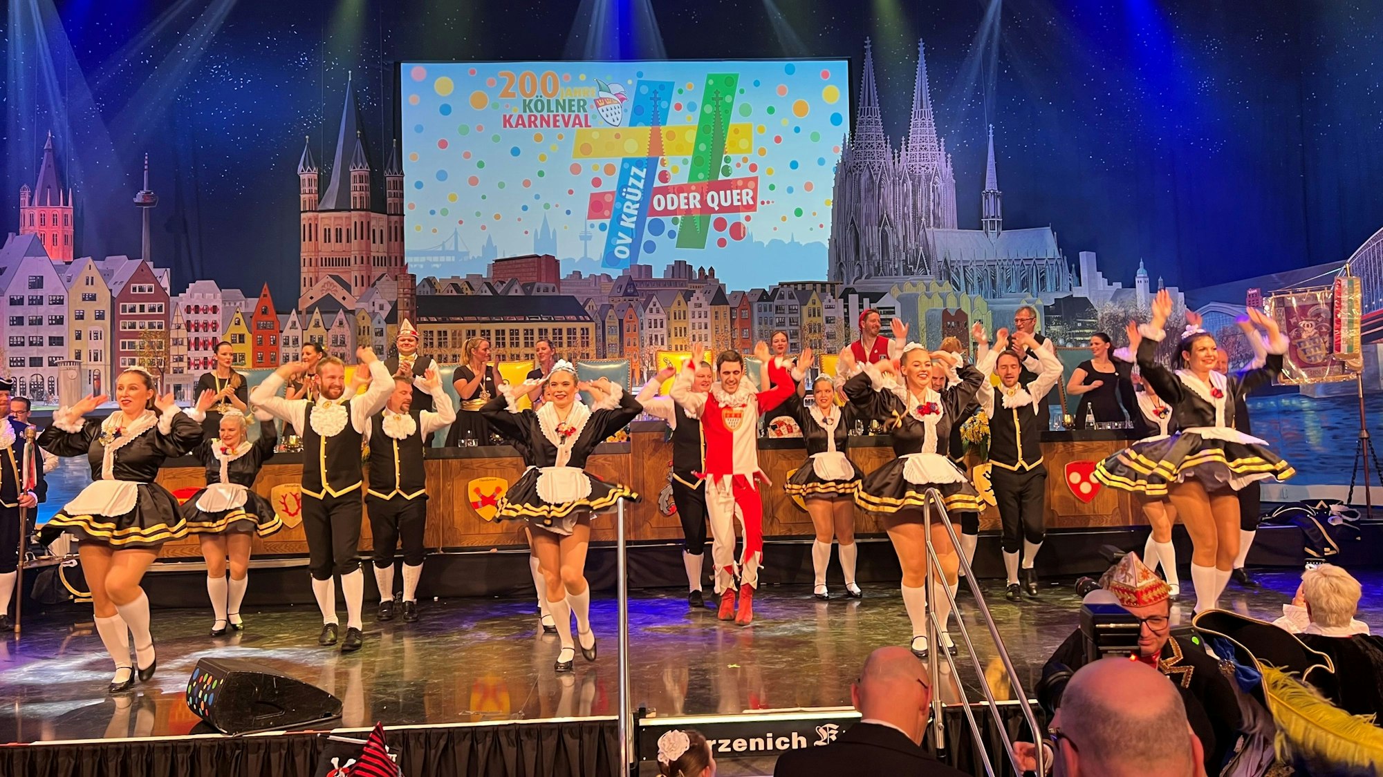 Viele karnevalistisch verkleidete Tänzer auf einer Bühne.