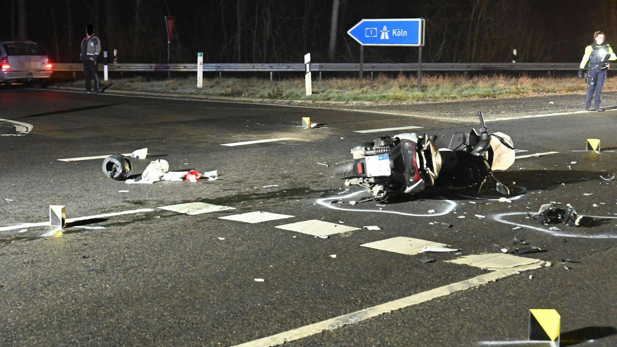 Ein schwer demolierter Roller liegt auf der Seite auf der Straße. Viele Einzelteile liegen drumherum. Sie sind mit Kreide von der Polizei markiert.
