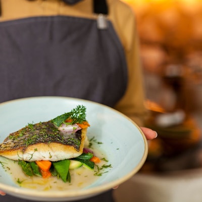 Ein Kellner serviert einen Teller mit einem Fisch-Gericht.
