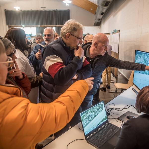 Männer und Frauen stehen in der Bürgerhalle Wiesdorf vor Bildschirmen.