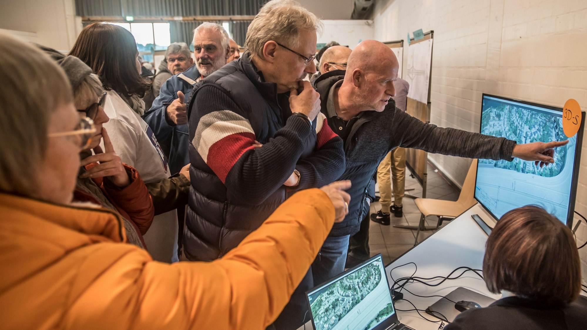 Männer und Frauen stehen in der Bürgerhalle Wiesdorf vor Bildschirmen.