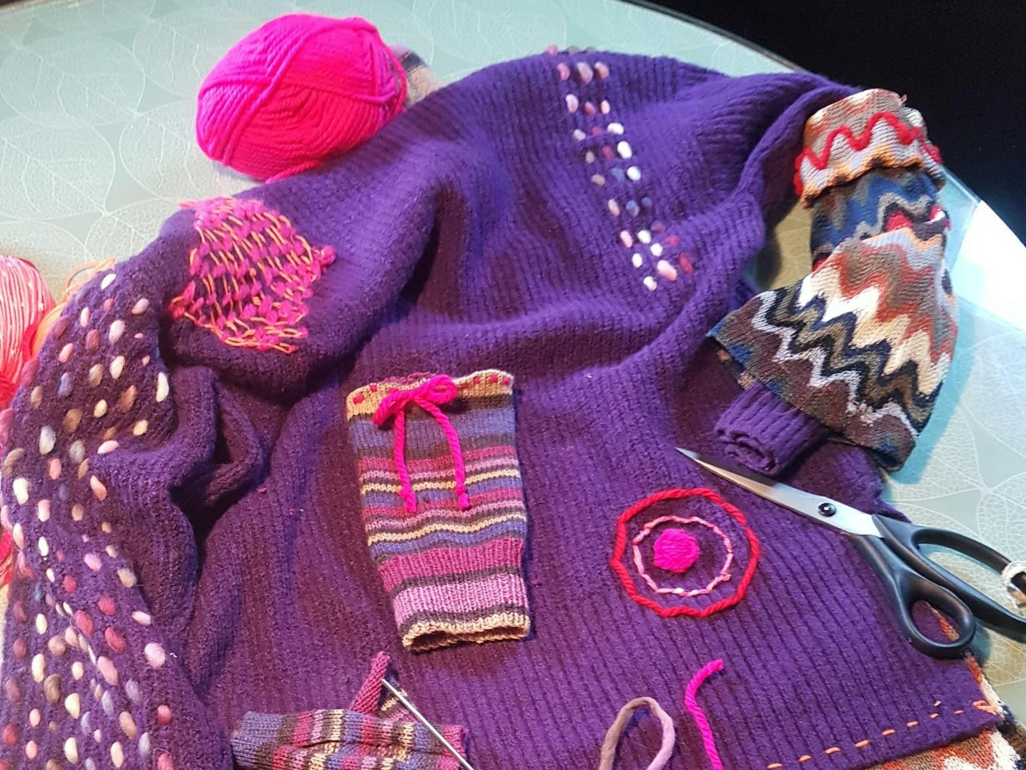 Ein lila Pullover ist mit bunten Mustern verziert.