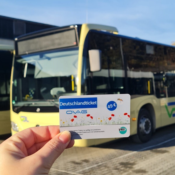 Eine Hand hält ein Tickets, im Hintergrund steht ein Bus.