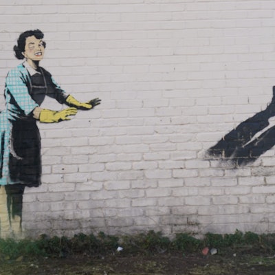 Das neue Kunstwerk des Straßenkünstlers Banksy mit dem Titel „Valentine's Day Mascara“ an der Seite eines Gebäudes wurde von einer Gefriertruhe und zerbrochenen Möbeln, die Teil der Installation waren, befreit. Das Kunstwerk zeigt eine Hausfrau aus den 1950er Jahren, die eine klassische blaue Krawatte und gelbe Spülhandschuhe trägt, mit einem geschwollenen Auge und einem fehlenden Zahn, die ihren männlichen Partner in eine Gefriertruhe zu schubsen scheint.