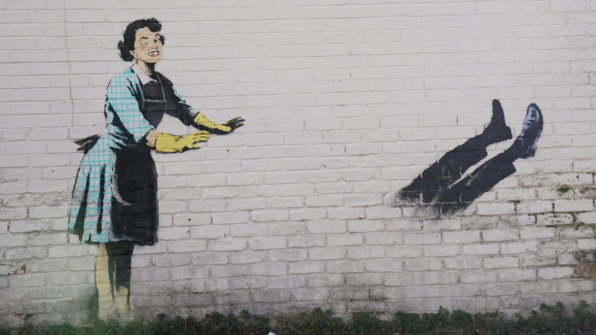 Das neue Kunstwerk des Straßenkünstlers Banksy mit dem Titel „Valentine's Day Mascara“ an der Seite eines Gebäudes wurde von einer Gefriertruhe und zerbrochenen Möbeln, die Teil der Installation waren, befreit. Das Kunstwerk zeigt eine Hausfrau aus den 1950er Jahren, die eine klassische blaue Krawatte und gelbe Spülhandschuhe trägt, mit einem geschwollenen Auge und einem fehlenden Zahn, die ihren männlichen Partner in eine Gefriertruhe zu schubsen scheint.