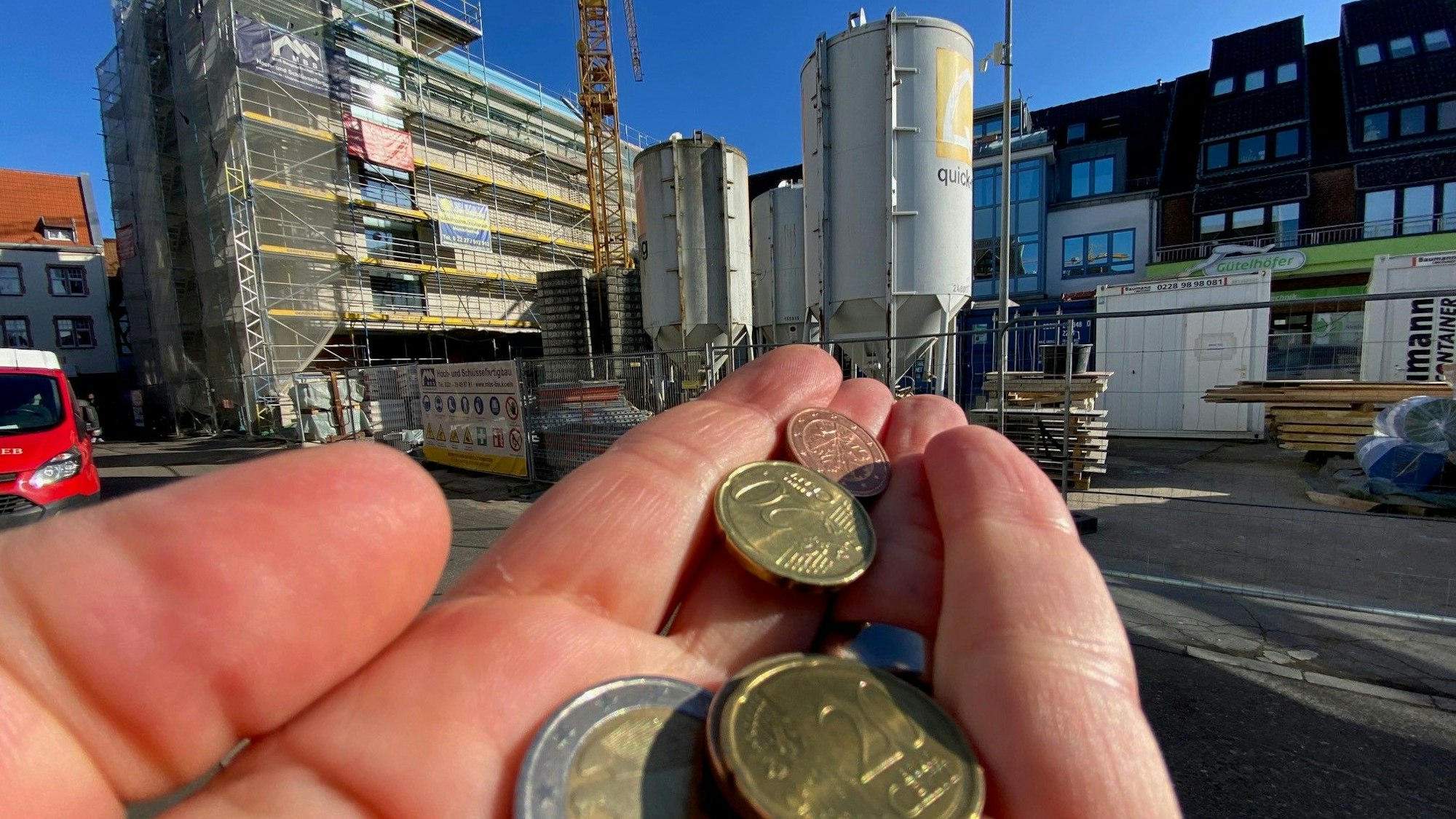 Eine Hand mit Münzen. Im Hintergrund sieht man die Baustelle des Brühler Rathaus. (Symbolbild)