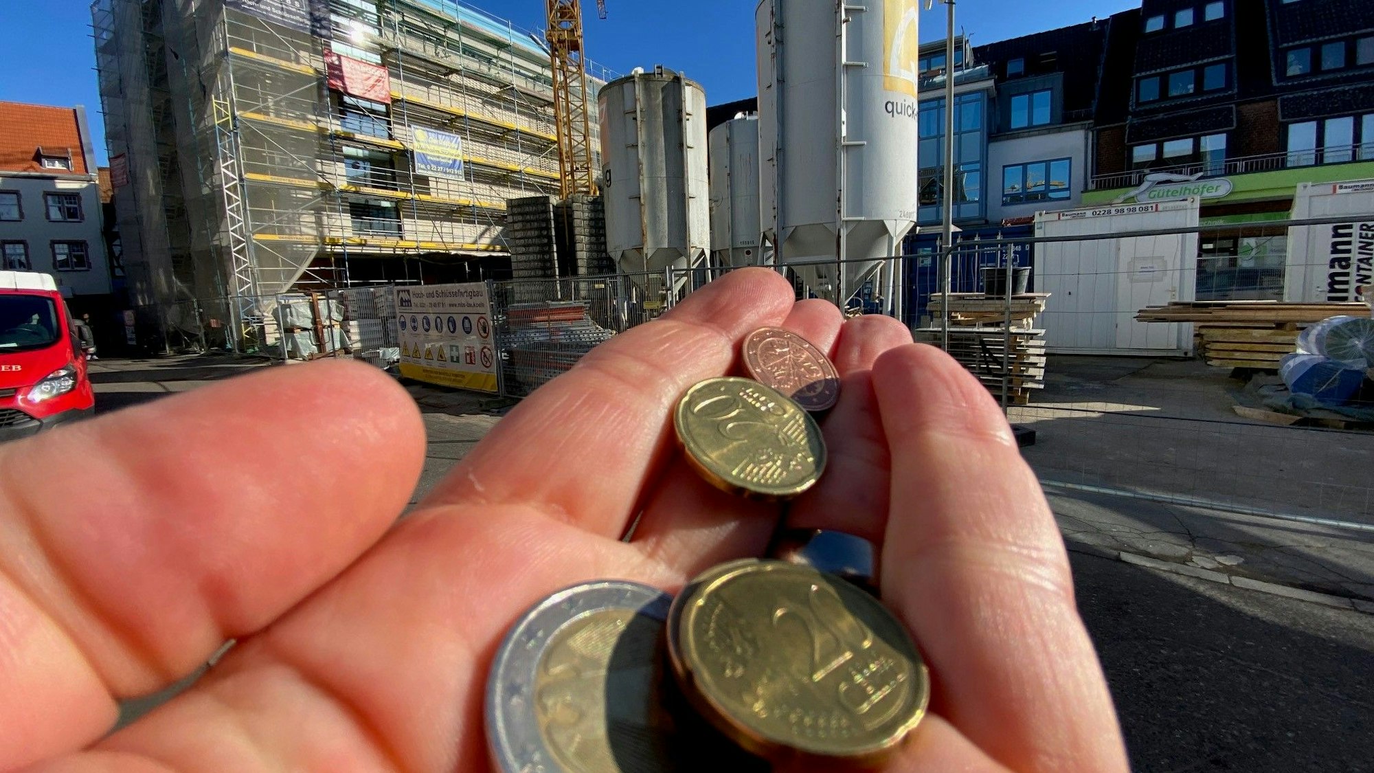 Eine Hand mit mehren Münzen vor dem Rathausbau in Brühl.