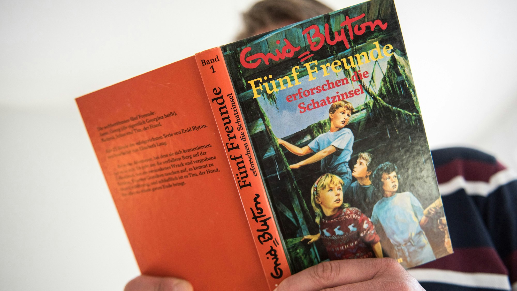 Ein Mann hält den ersten Band der Abenteuerserie "Fünf Freunde" von Schriftstellerin Enid Blyton in der Hand