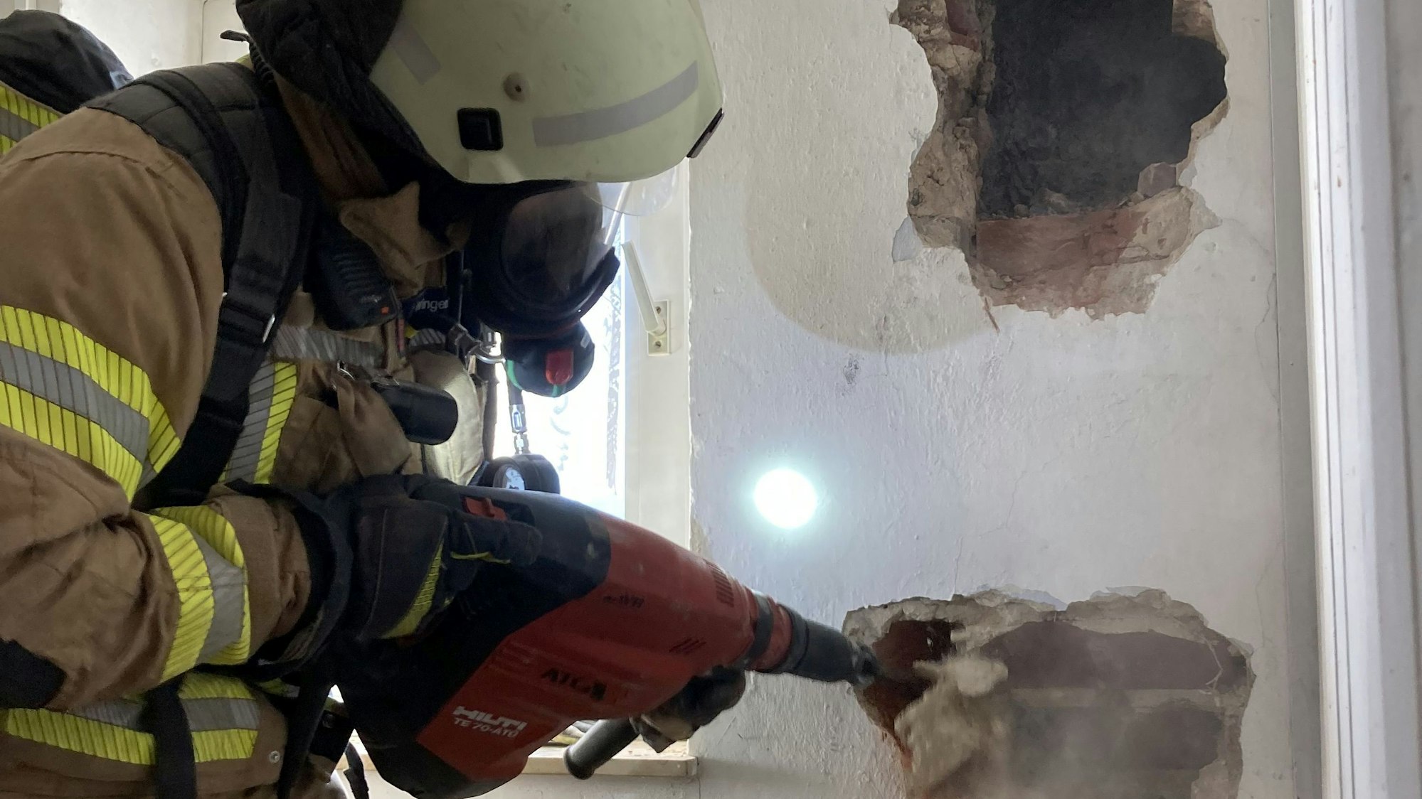 Ein Feuerwehrmann öffnet eine Wand mit einem Stemmhammer.