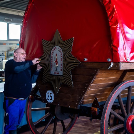 Das Bild zeigt den historischen Planwagen der Prinzengarde. Ein Mann montiert gerade ein Schild.
