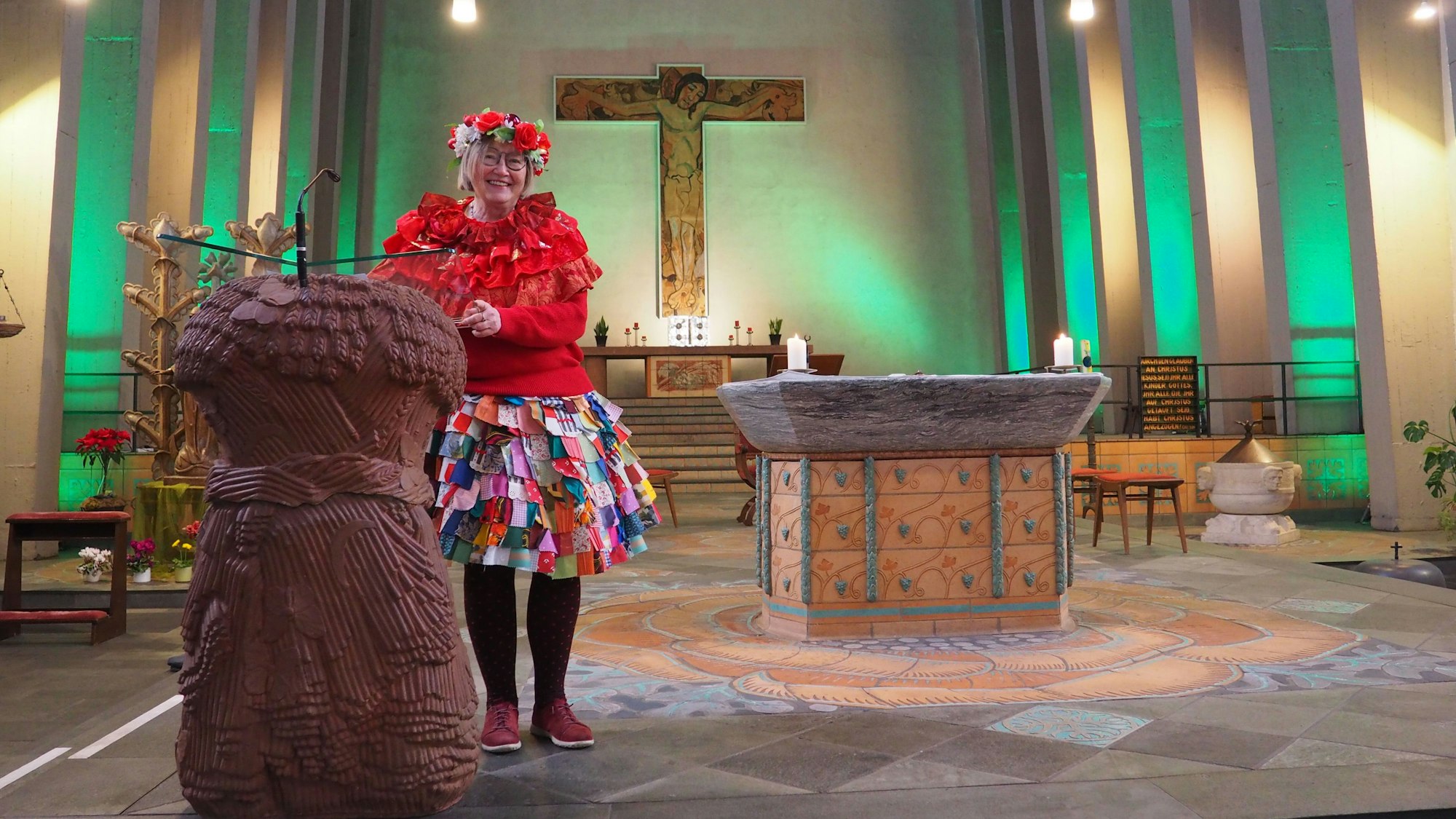 Gertrud Brück-Gerken steht am Pult vor dem Altar in der Kirche mit Lappenclown-Rock und buntem Blumenkranz im Haar.
