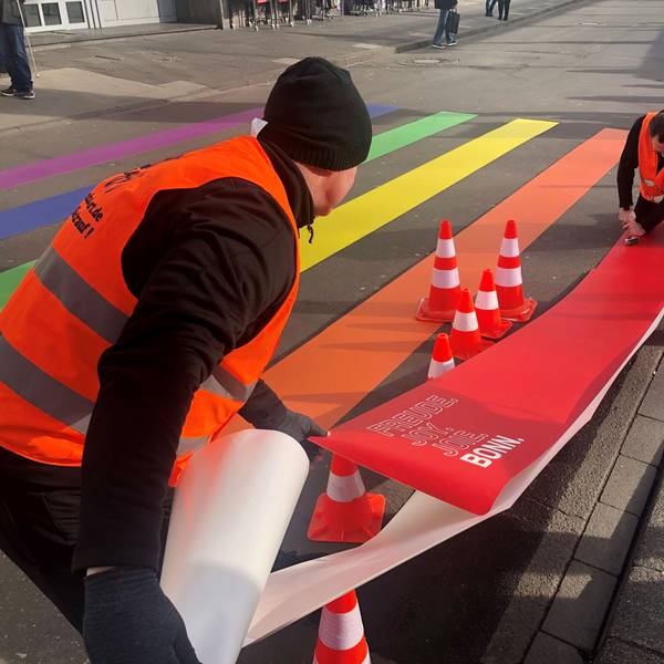 Zwei Menschen befestigen bunte Zebrastreifen auf der Straße.