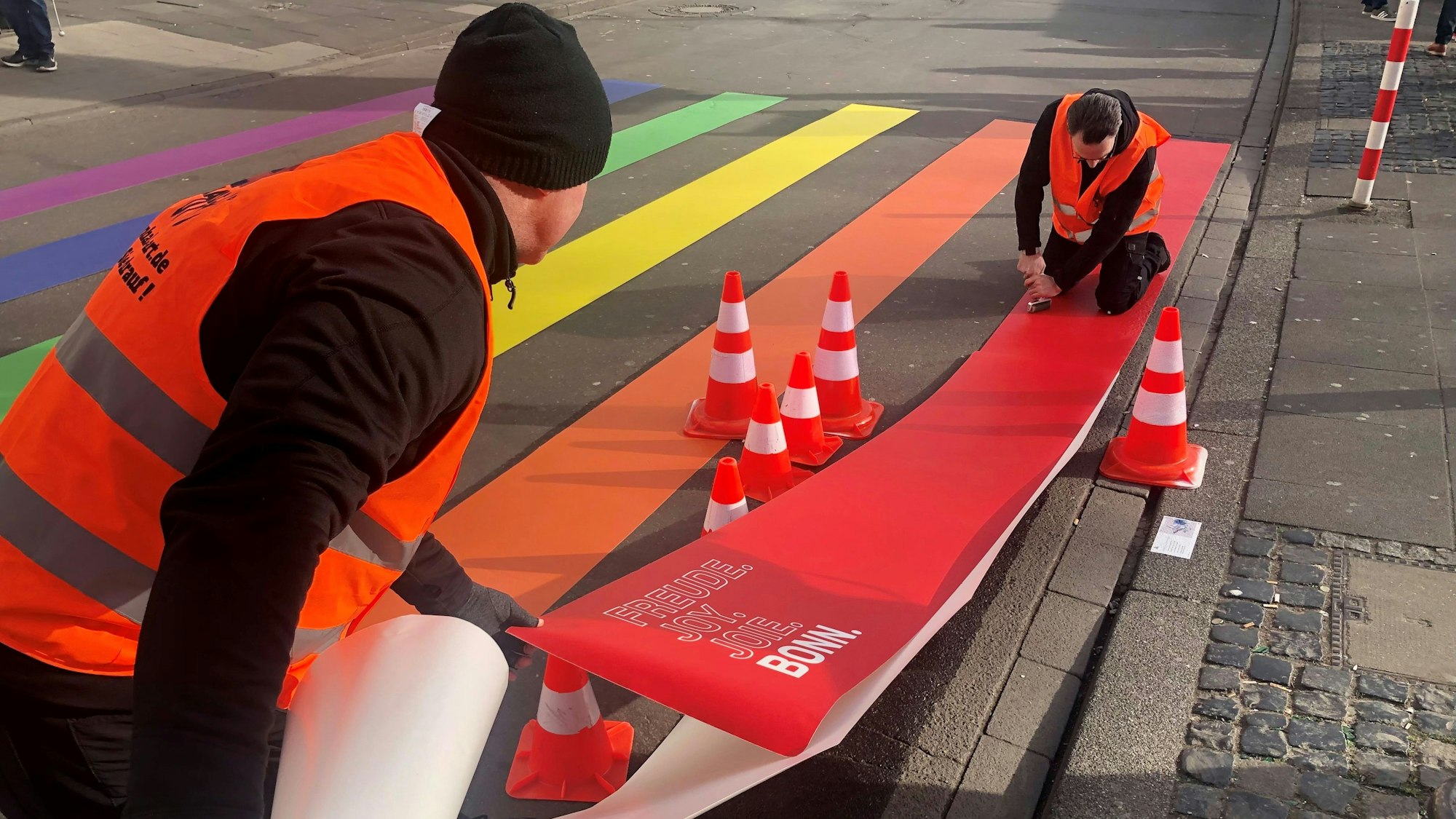 Zwei Menschen befestigen bunte Zebrastreifen auf der Straße.