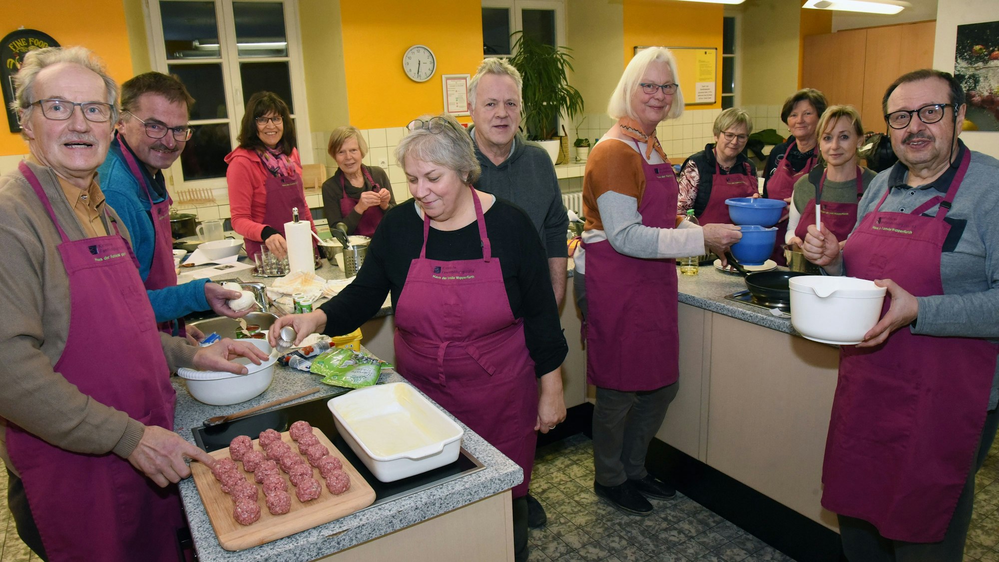 Mehrere Personen mit roten Schürzen stehen in einer großen Küche und sind Essen am Zubereiten.