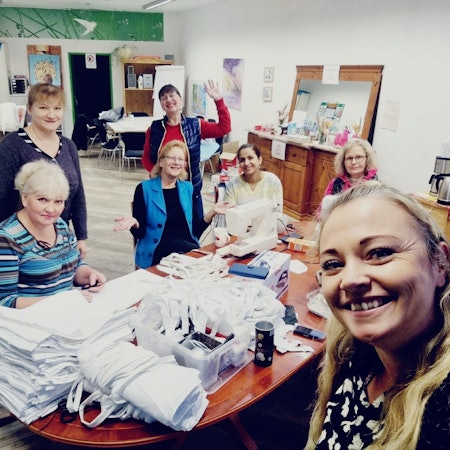 Mehrere Frauen sitzen an einem Tisch und nähen die Kostüme.