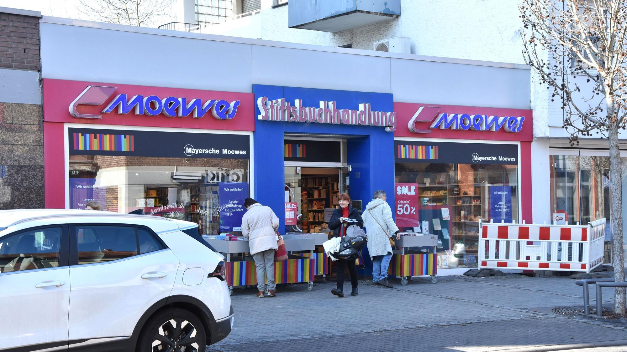 Das Foto zeigt die Stiftsbuchhandlung an der Hahnenstraße in Kerpen. Eine Kundin verlässt das Geschäft, zwei Frauen stöbern in Bücherkisten.