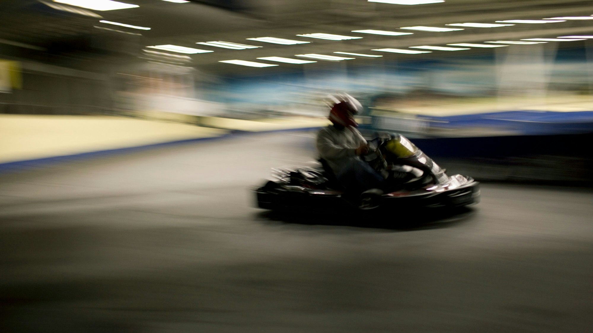 Eine Person mit einem Helm sitzt in einem Kart. Das Bild ist leicht verschwommen.