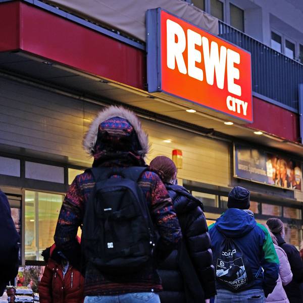 Menschen stehen vor einem Rewe-Supermarkt in Köln.