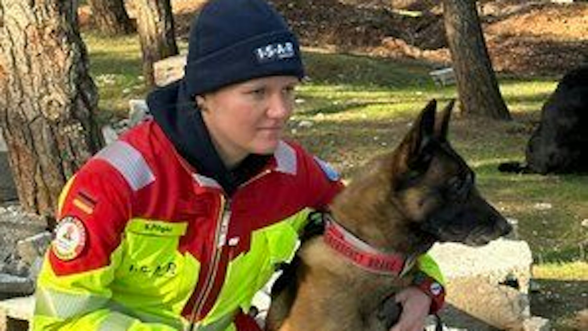 Sandra Pilger geht neben ihrem Hund Hero in die Hocke. Sie trägt eine schwarze Mütze.