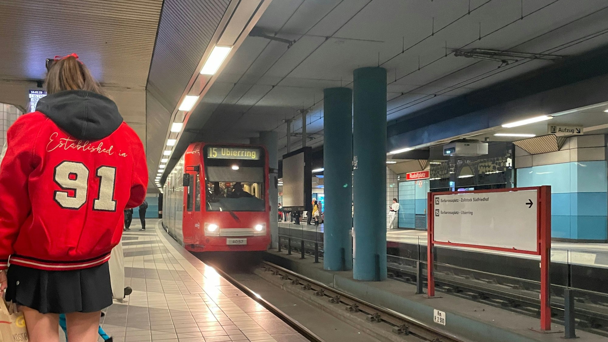 Eine Bahn der Linie 15 fährt am Rudolfsplatz ein. Verkleidete Karnevalisten warten am Gleis.
